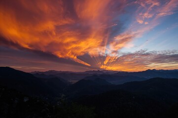 Wall Mural - Stunning fiery sunset over rugged peaks. Scenic view with sunlight piercing vibrant orange clouds