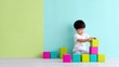 © Дмитрий Баронин - Young Asian boy is stacking colorful building blocks on a light wooden floor, surrounded by vibrant pastel walls, showcasing creativity and playfulness in a bright environment