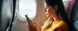 © PixelNexusArt - Young freelance woman using smartphone inside airplane seat with natural light from window creating calm mood