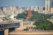A tall tower sits on a green hill overlooking a city next to the Yangtze River in China.