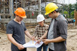 © skarie - Team of engineers and architects wearing safety helmets discussing building progress at construction site with scaffolding structure.