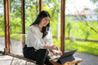 © Apichat - woman is sitting on a chair in front of a laptop. She is smiling and she is enjoying her time. The scene suggests a relaxed and comfortable atmosphere