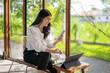 © Apichat - woman is sitting on a chair with a laptop and a cell phone in front of her