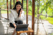 © Apichat - woman is sitting at a table with a laptop and a cell phone