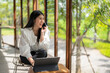 © Apichat - woman is sitting at a table with a laptop and a cell phone