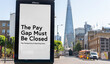 Billboard reading “The pay gap must be closed” with The Shard and city skyline, London, UK