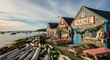 © Arisara - Picturesque Maine coastal village featuring vibrant fishing shacks, quaint picnic tables, and boats in the tranquil harbor under a beautiful sky, capturing New England's unique charm