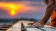 © Rouf - Close-up view of hardworking construction worker's hands resting on wooden beams at sunset, showcasing the dedication and effort in outdoor construction.