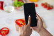 © Prostock-studio - Social networks at home, mobile app and cooking with gadget. Millennial african american female use smartphone with blank screen in kitchen, at table with bright vegetables background, pov, mockup