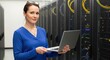 © tahir xh - Confident woman in blue shirt holding laptop in a server room with racks of equipment.