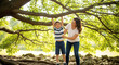 © Marcela - Happy child hanging from tree branch with mother in park