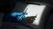 © photoplotnikov - Gloved hand holding syringe over white pillow in dimly lit room