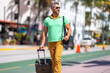 A tourist with luggage on streets in tropical city. A man traveler tourist on summer vacation. Tourist with suitcase on summer city. Man tourist walk on city. Travel lifestyle. Summer weekend getaway.