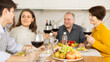 © JackF - Cheerful young girl sitting at table with husband and senior parents during cozy family celebration over kitchen table served with wine and light snacks