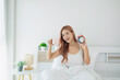 © WMSTUDIO - Smiling young woman in bed holding cup of coffee and alarm clock, enjoying morning routine in bright and cozy bedroom with modern decor