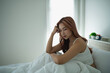 © WMSTUDIO - Young woman sitting on bed with thoughtful expression, morning light pouring through window, cozy bedroom atmosphere, contemplating thoughts alone