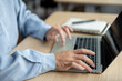 © bongkarn - Close up of a man's hands typing on laptop aside notebook while sitting at wooden table in a cafe.