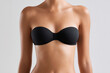 © Nyxoria - A woman's tanned torso wearing a black strapless bra against a neutral background. Beauty and body positivity in simple elegance.