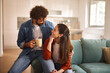 © Stockphotodirectors - A man and woman share a warm moment in a stylish living room. They smile at each other, holding a coffee mug, surrounded by soft furnishings and natural light.