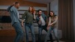 © Yuliia - Happy multiracial four diverse people friends dancing energetic at home party smiling relaxing ethnic millennials free men women laughing dance funny having fun listening music moving in living room