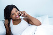 © wavebreak3 - African American woman reclining in bed in bedroom holding smartphone and displaying ring on finger