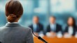 © LarisaM - A woman is standing in front of a group of people, possibly giving a speech. Concept of authority and professionalism, as the woman is dressed in a suit and tie and is holding a microphone