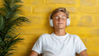 © siraphol - Relaxing teenager enjoying music with headphones against vibrant yellow wall