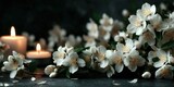 Close-up of white jasmine flowers with soft petals, two lit candles on a dark background