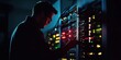 © Darren - A silhouette of a technician working on hardware inside a dimly lit server room. The glowing lights from the server racks highlight the technological environment and critical operations