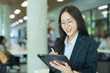© maeching - Asian businesswoman standing in front of modern business building and using tablet to work.