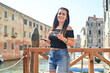 Happy smiling beautiful  Tourist  woman traveling at   Venice Italy, poses and making photos   against colorful houses. Concept of Italian gastronomy and travel. 