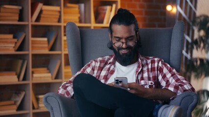 Young Indian man in eyeglasses texting on smartphone at home, social networks