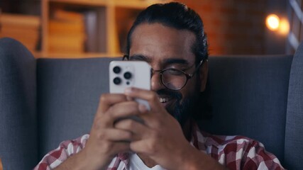 Joyful Indian man in glasses chatting on smartphone, enjoying social network