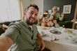 © AnnaStills - Portrait of Caucasian young adult man taking selfie with smiling Caucasian senior woman, Caucasian young adult woman, two Caucasian children celebrating birthday at dining table
