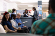 © DC Studio - Asian male patient completes medical registration as hospital receptionist explains clipboard healthcare forms in clinic lobby. Young man preparing for doctor appointment in emergency waiting room.