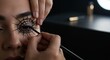© Sergiy - A detailed close-up of a young adult's eye featuring an intricate black spider web design being carefully applied by a skilled makeup artist's hands in a dimly lit setting.