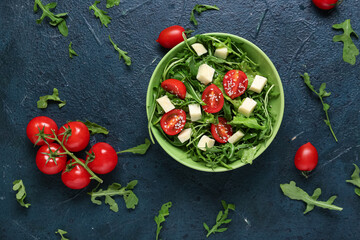 Wall Mural - Bowl with tasty arugula salad and ingredients on blue grunge background