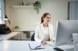 © Stella 16 - A woman is sitting at a desk in office with a computer monitor in front of her. She is smiling and she is enjoying her work