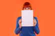 © Iryna - Young woman in blue sweater holds blank paper in front of her face against vibrant orange background during creative photo shoot