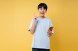 © Q88 - Excited young man using smartphone pointing up with a bright yellow background Studio shot