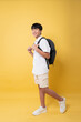 © Q88 - A smiling student with a backpack ready for school stands against a vibrant yellow backdrop