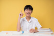 © Q88 - Excited student with a eureka moment raising a finger at a desk full of school supplies