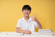 © Q88 - Student studying and giving a thumbs up sitting at a desk against a yellow background
