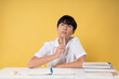 © Q88 - Teen student ponders a question pen in hand with notebooks and books on a yellow background