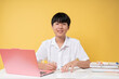 © Q88 - Young student focused on studying using a laptop and taking notes against a yellow background