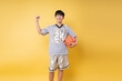 © Q88 - Young basketball player celebrating success holding ball wearing jersey number 24 on yellow backdrop