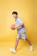 © Q88 - Teen basketball player dribbling an orange ball in front of a sunny yellow backdrop