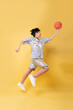 © Q88 - Teen basketball player in gray jersey leaps with ball in hand against a yellow background