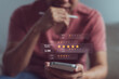 © thanmano - Checking customer feedback and five-star online reviews on smartphone with virtual interface for digital trust, brand reputation, and consumer experience