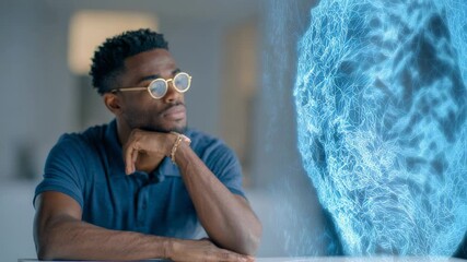 Software engineer with glasses and a blue shirt sits thoughtfully at a white table, observing a growing blue brain hologram made of interconnected lines